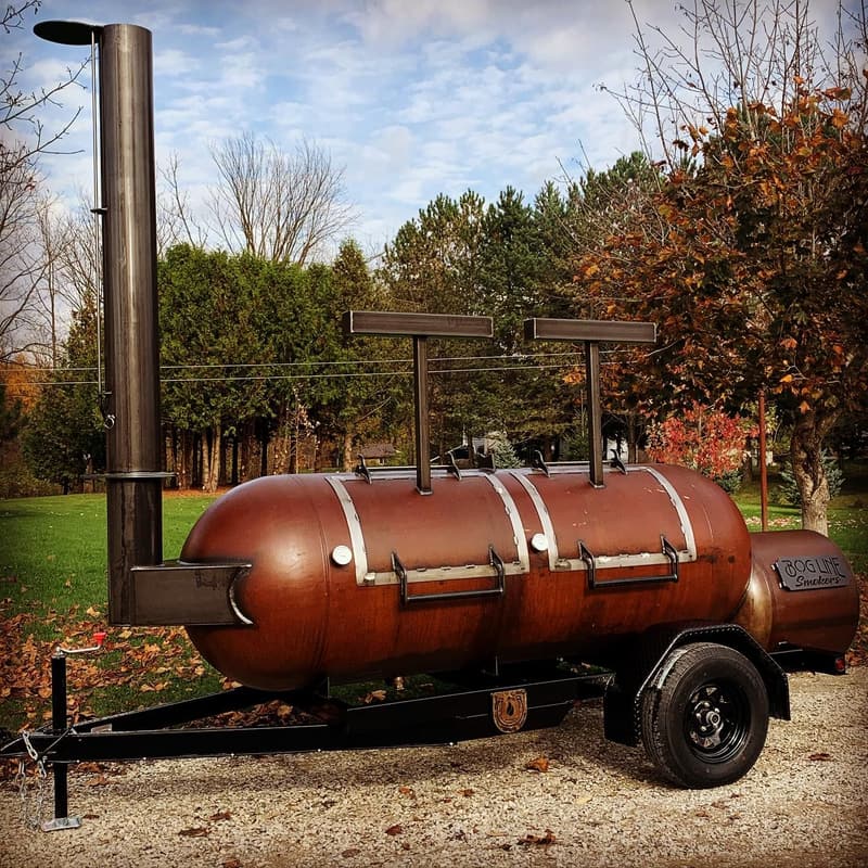 Patina offset smoker with a tall stack and counterweighted lids against autumn trees
