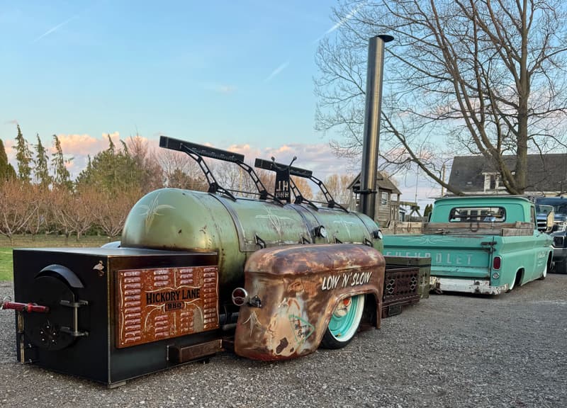 Hickory Lane BBQ's patina air-ride offset smoker with 'Low N Slow' fender, parked beside a teal Chevrolet C10